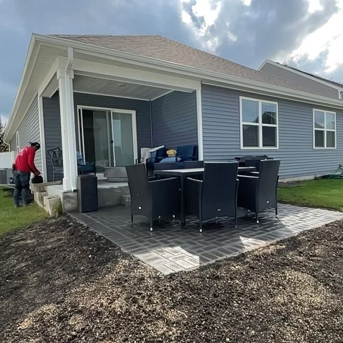 Back patio with covered porch, outdoor dining table and chairs, and two people working near the house.