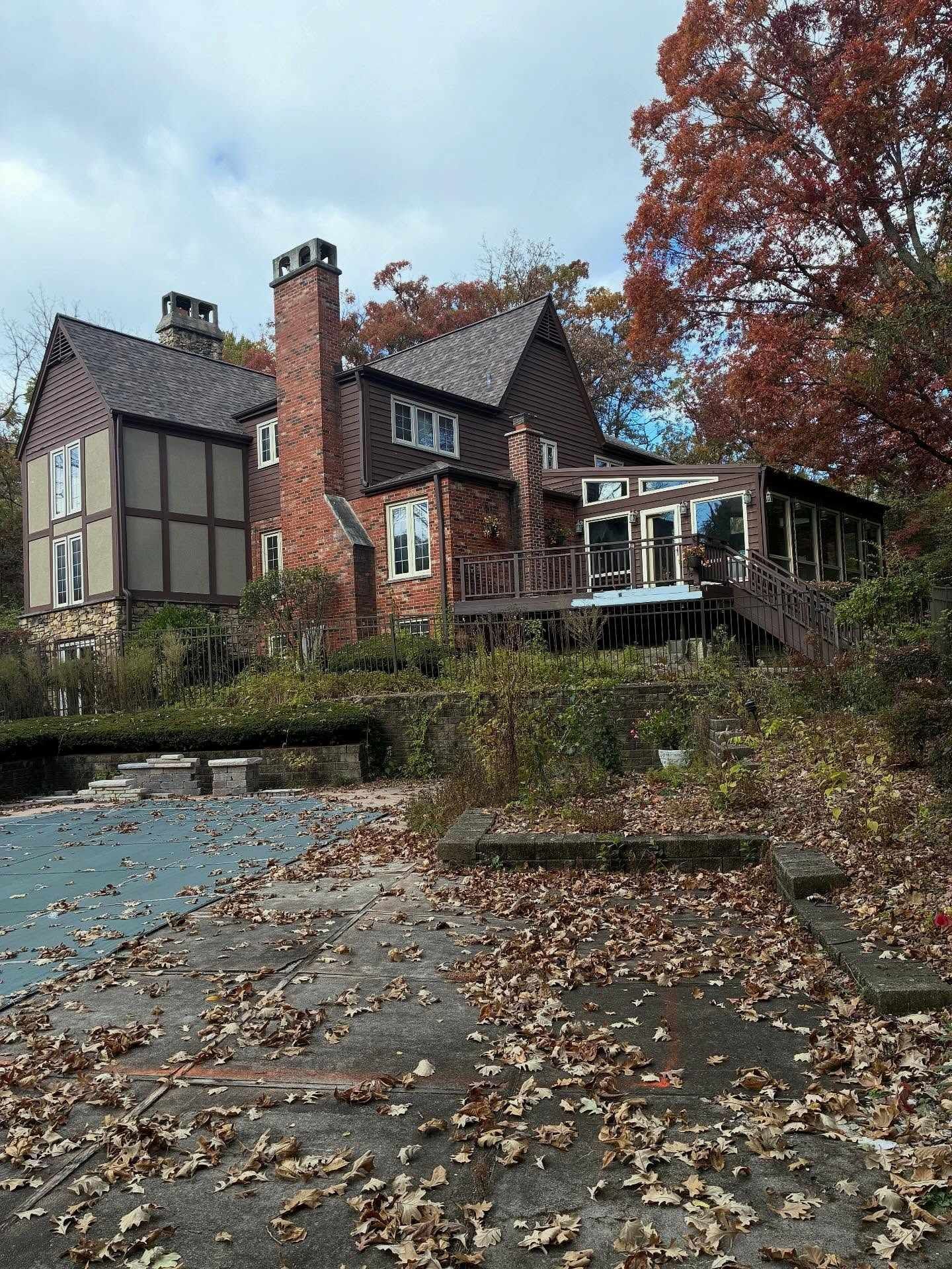 Autumn view of a brick-and-timber house with chimney, porch, and fallen leaves in the foreground