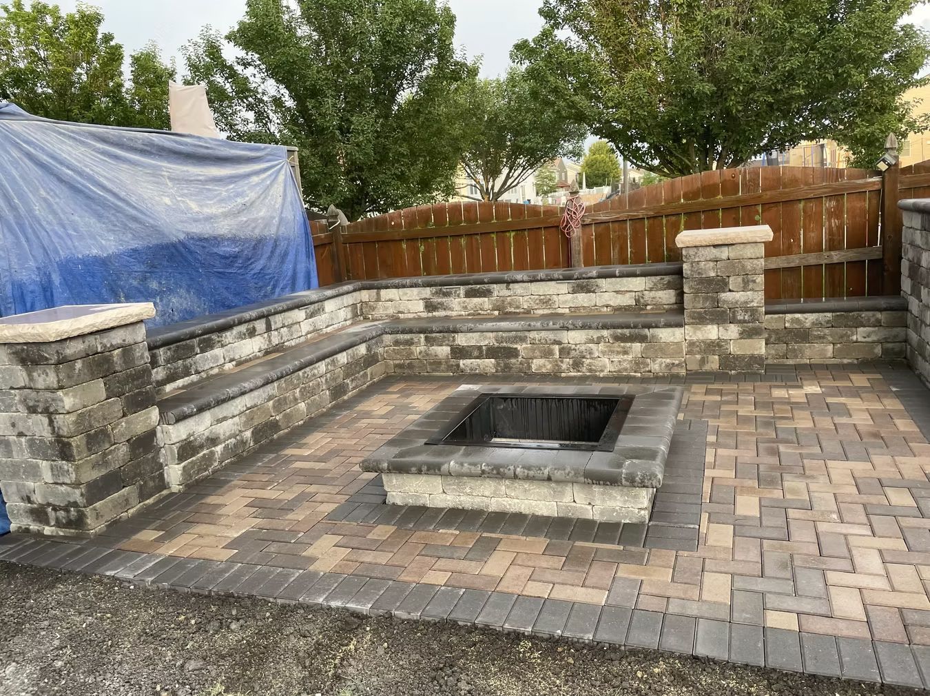 Stone backyard fire pit patio with paver flooring and wooden fence under overcast sky