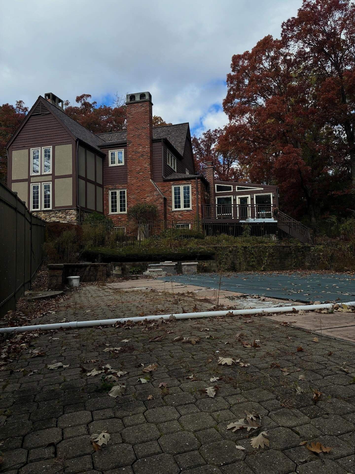 Old stone-and-timber house beside a pond, with autumn trees and a cobblestone foreground.