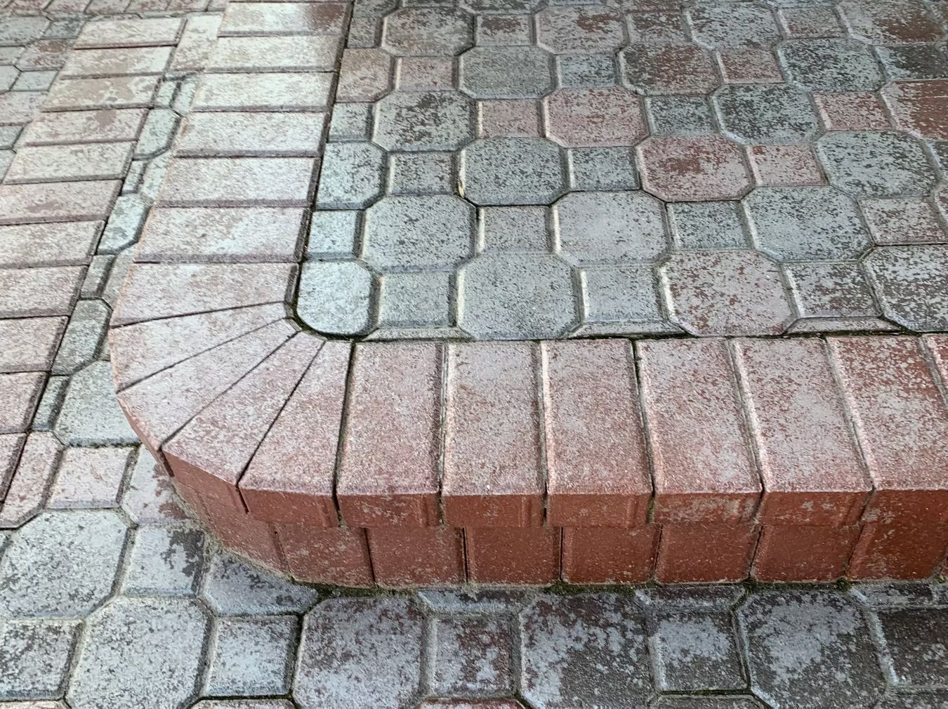 Curved brick step bordering a paved walkway of gray and pink cobblestones.
