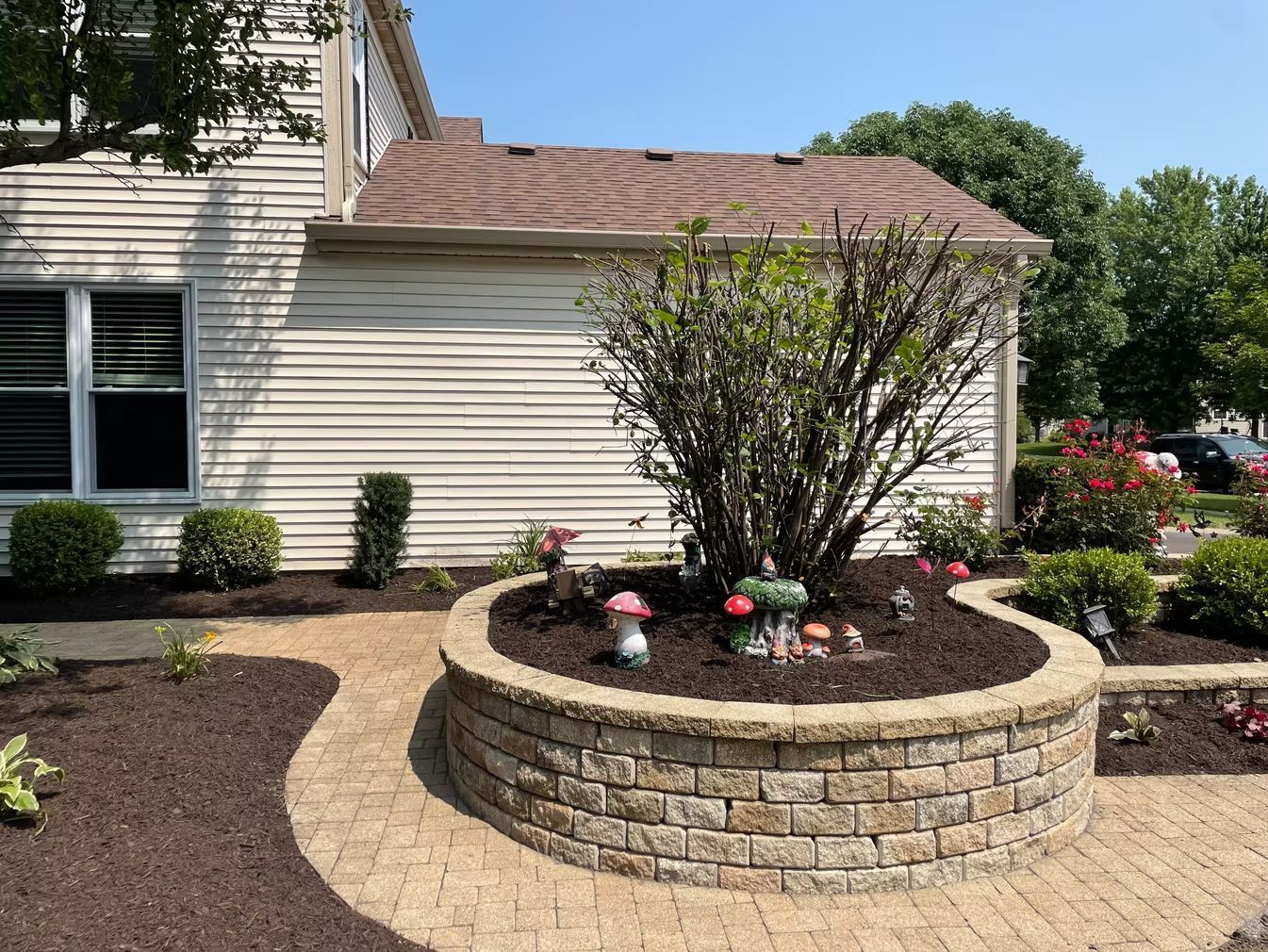 Landscaped front yard with a raised stone flower bed, shrubs, and a beige house exterior