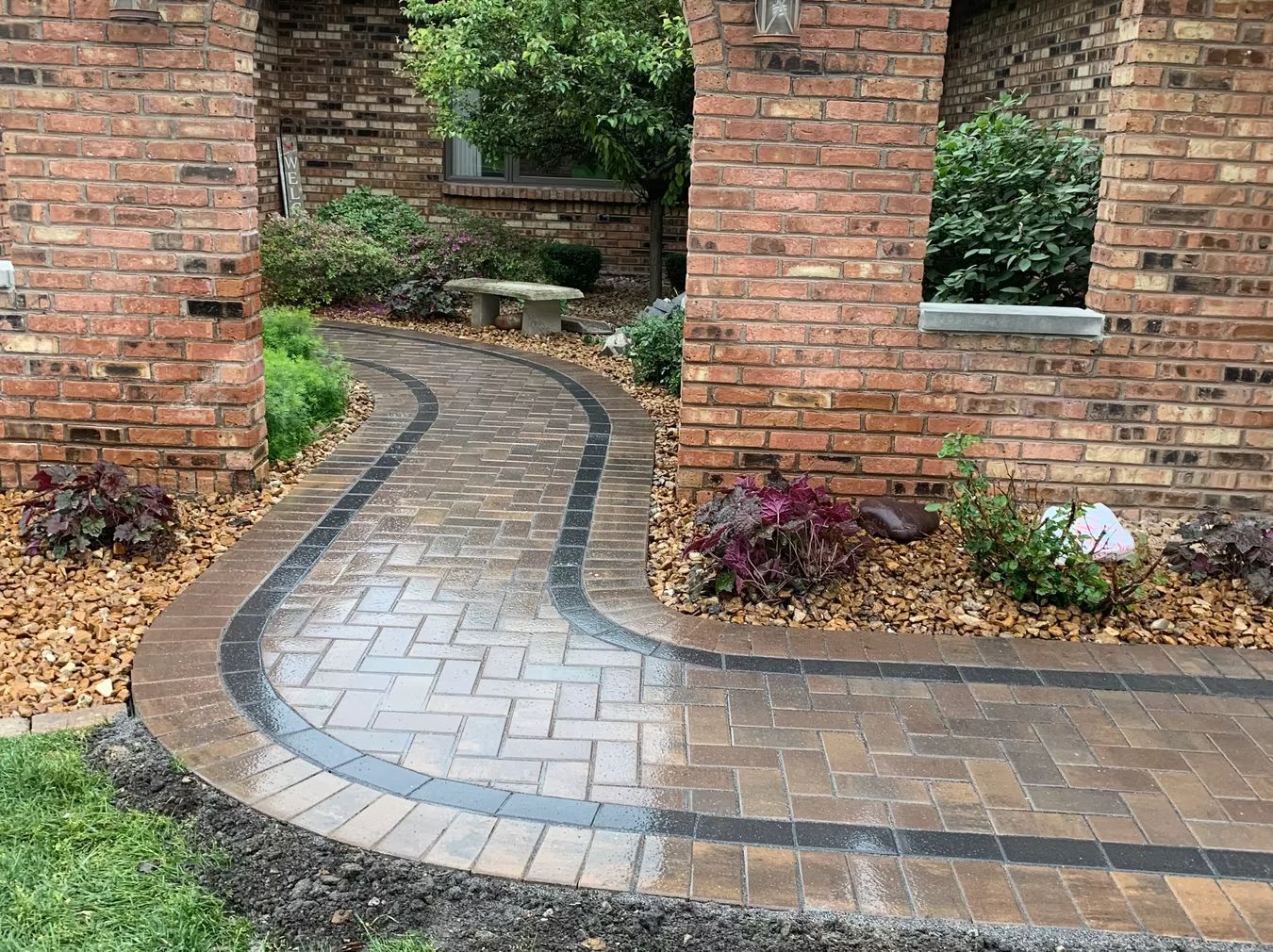 Curving brick walkway through a brick garden wall opening with shrubs and plants