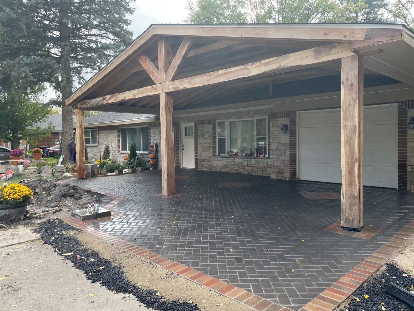 Covered brick driveway and house entrance with wood beams and a garage door under a porch.