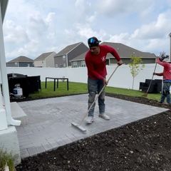 Worker leveling paver patio in a backyard, with another worker in the background.