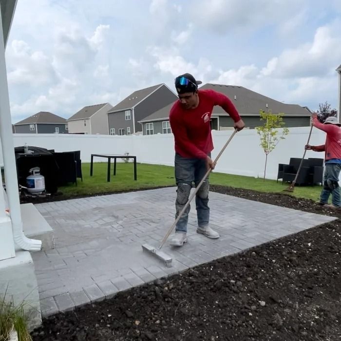 Worker smoothing a gray patio slab in a backyard with a roller tool