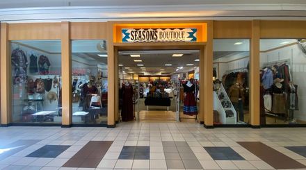 Storefront entrance with glass doors and windows, displaying clothing inside and a sign above the entrance.