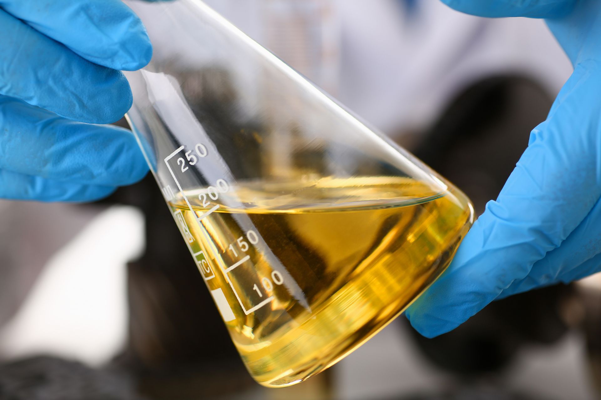 A person is holding a beaker with a yellow liquid in it.