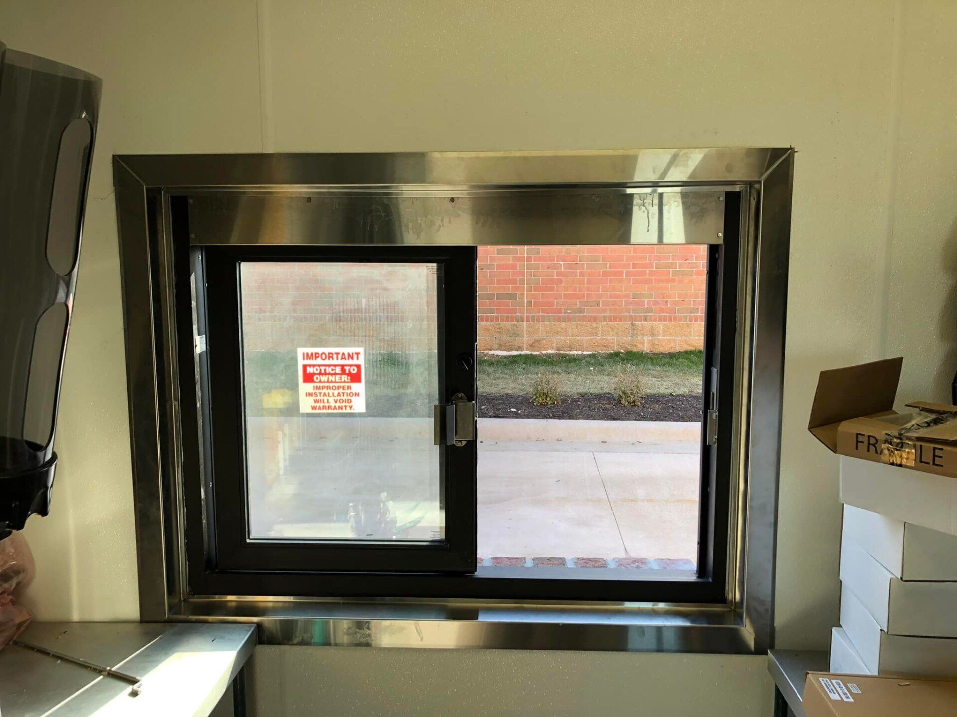 Small sliding window with frosted pane in a room, showing a sidewalk and brick wall outside.