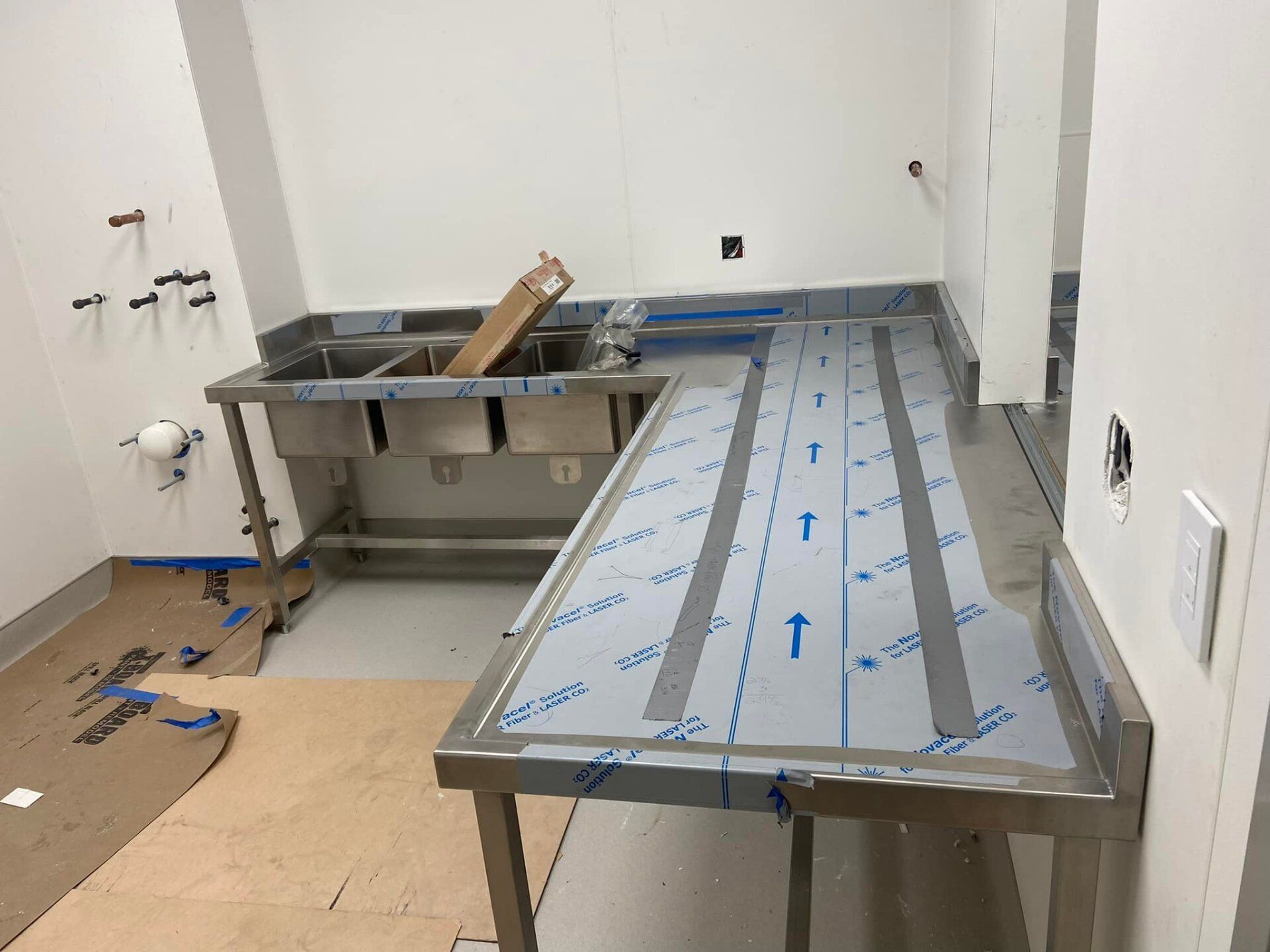 Kitchen under construction with metal countertops and unfinished flooring, plastic protection on surfaces.