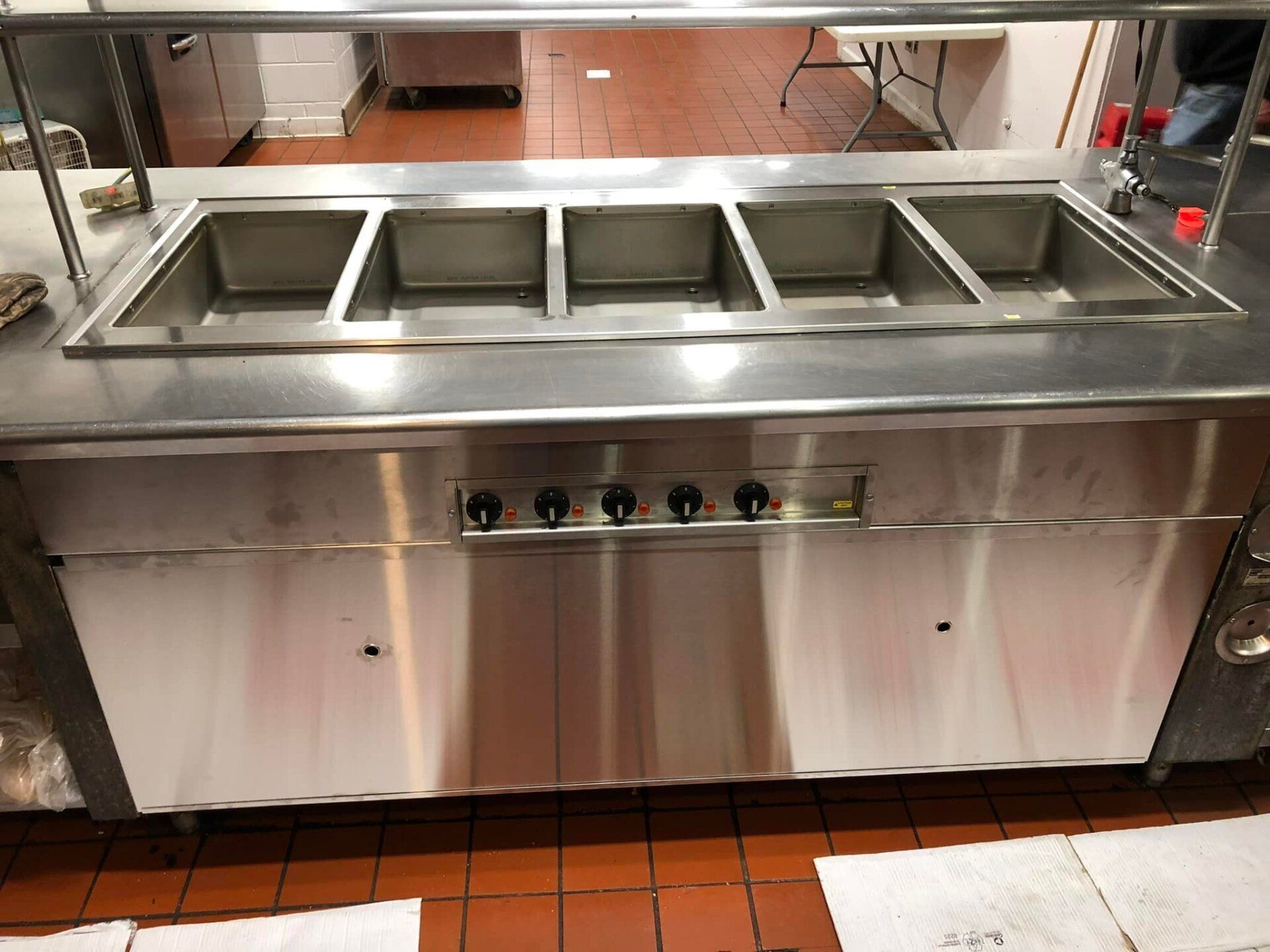 Stainless steel commercial food prep station with four ingredient bins and undercounter storage on red tile floor