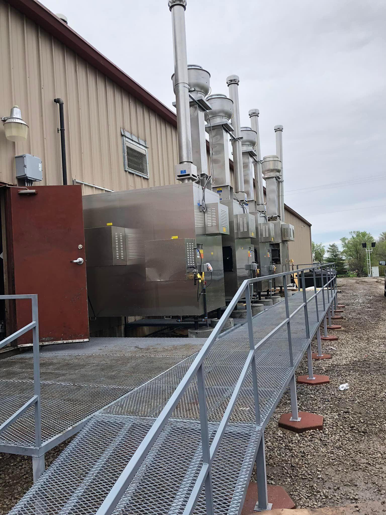 Industrial machinery beside a metal building, with a fenced gravel service path in front.