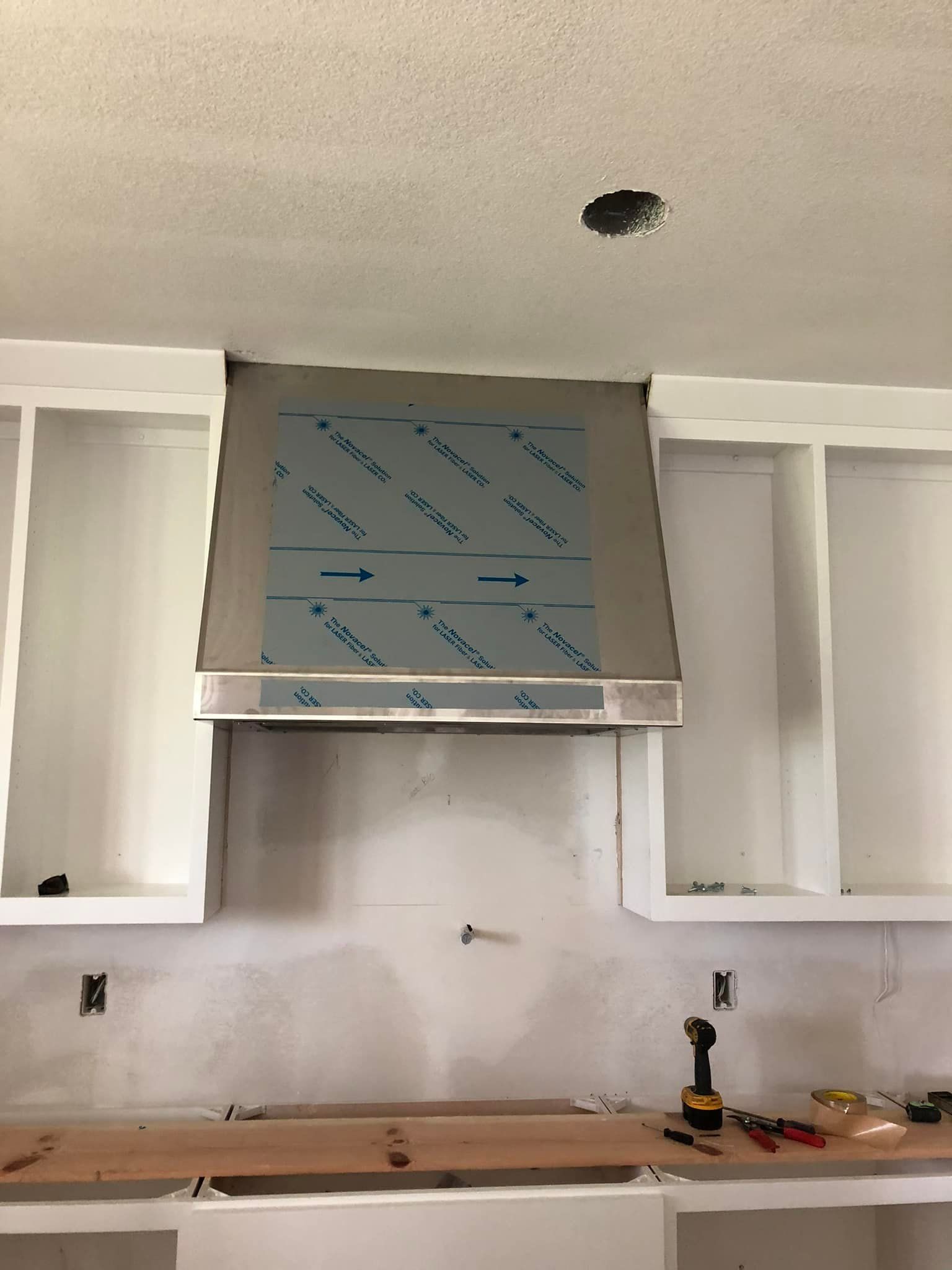 Kitchen under renovation with white cabinets, gray range hood, and uncovered countertop.