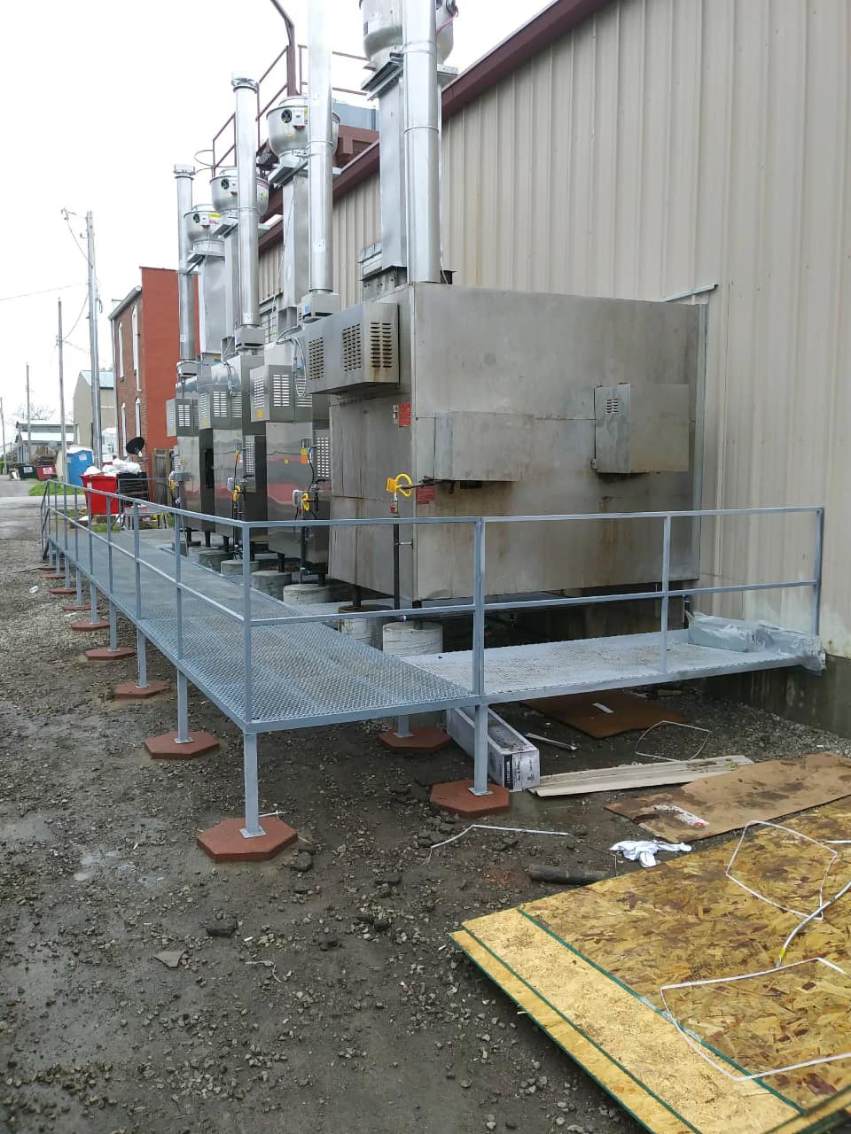 Industrial equipment on a metal walkway beside a building, with gray machinery and railings.