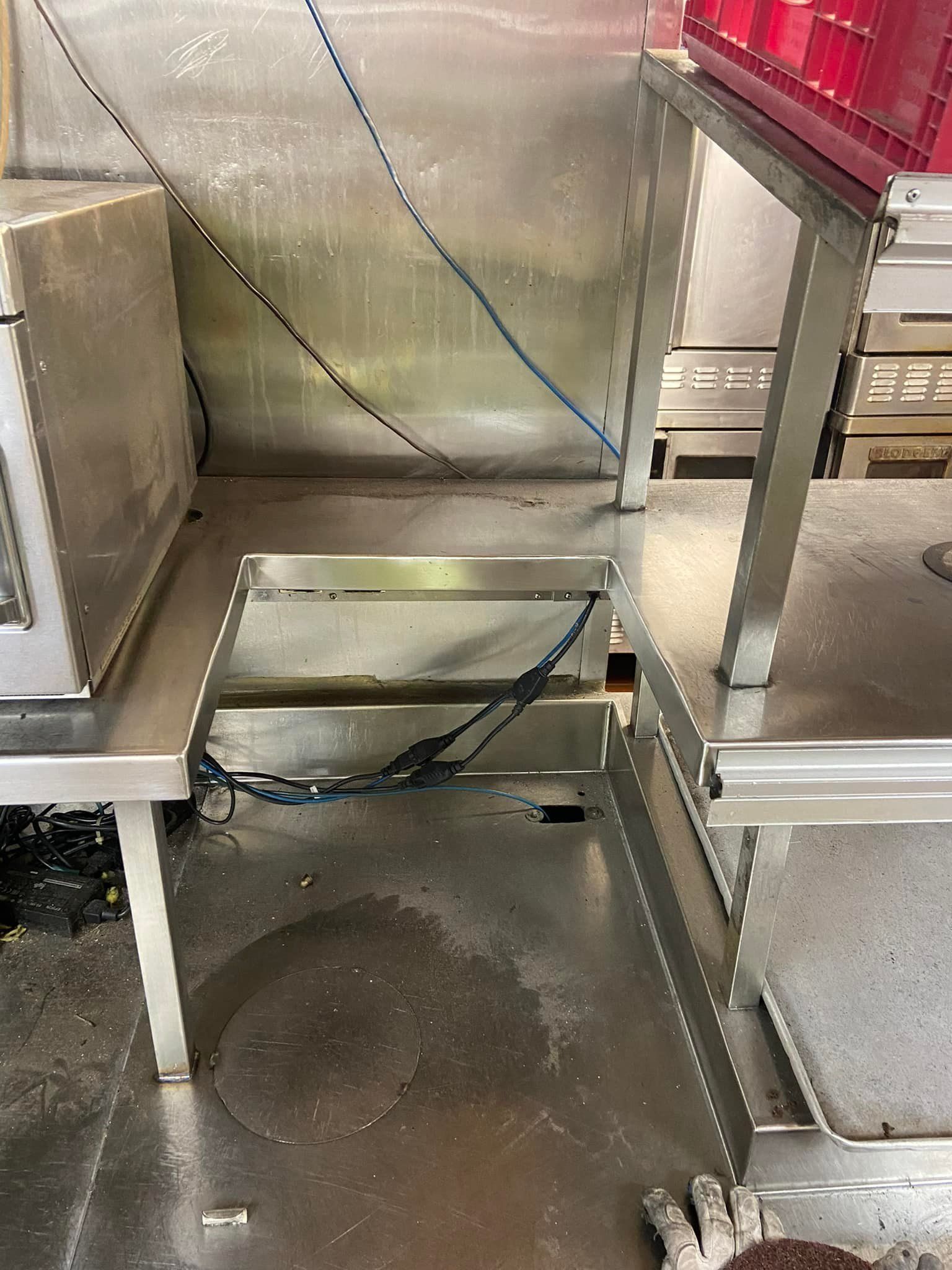 Open floor hatch beside metal equipment in an industrial kitchen area.