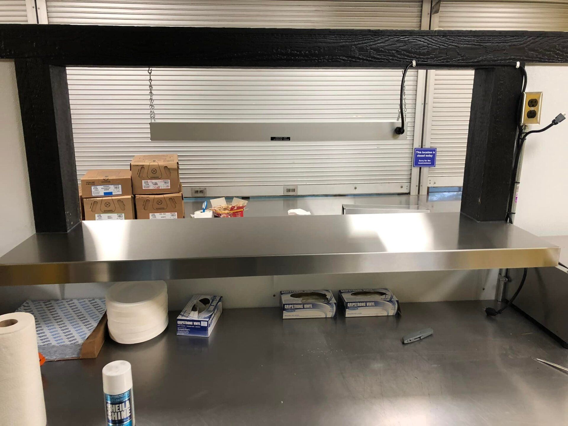 Kitchen pass-through counter with a metal shelf, paper towels, and cleaning supplies on a stainless steel surface