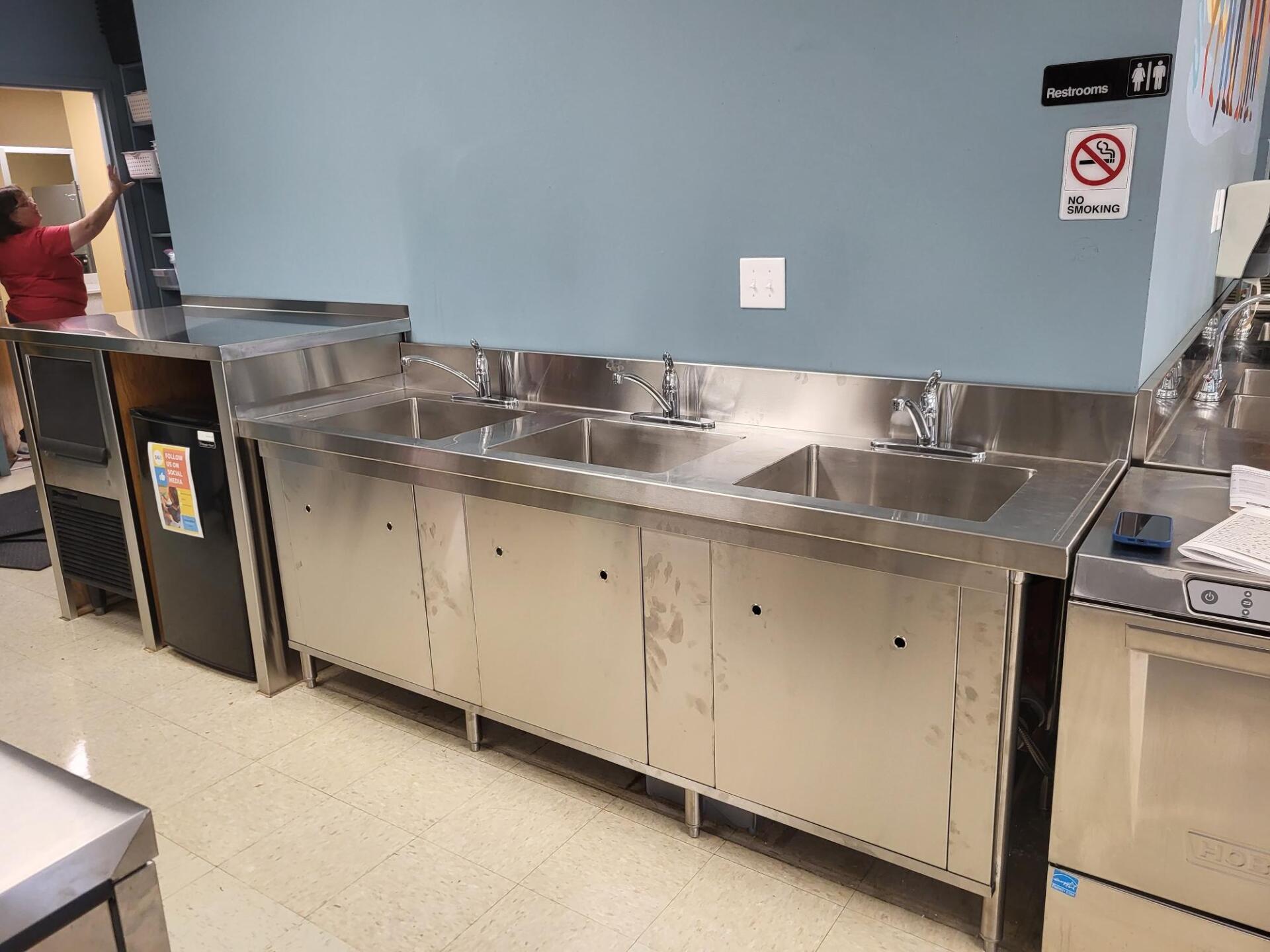 Commercial kitchen stainless-steel prep counter and cabinets along a blue wall, with sink and counter equipment.