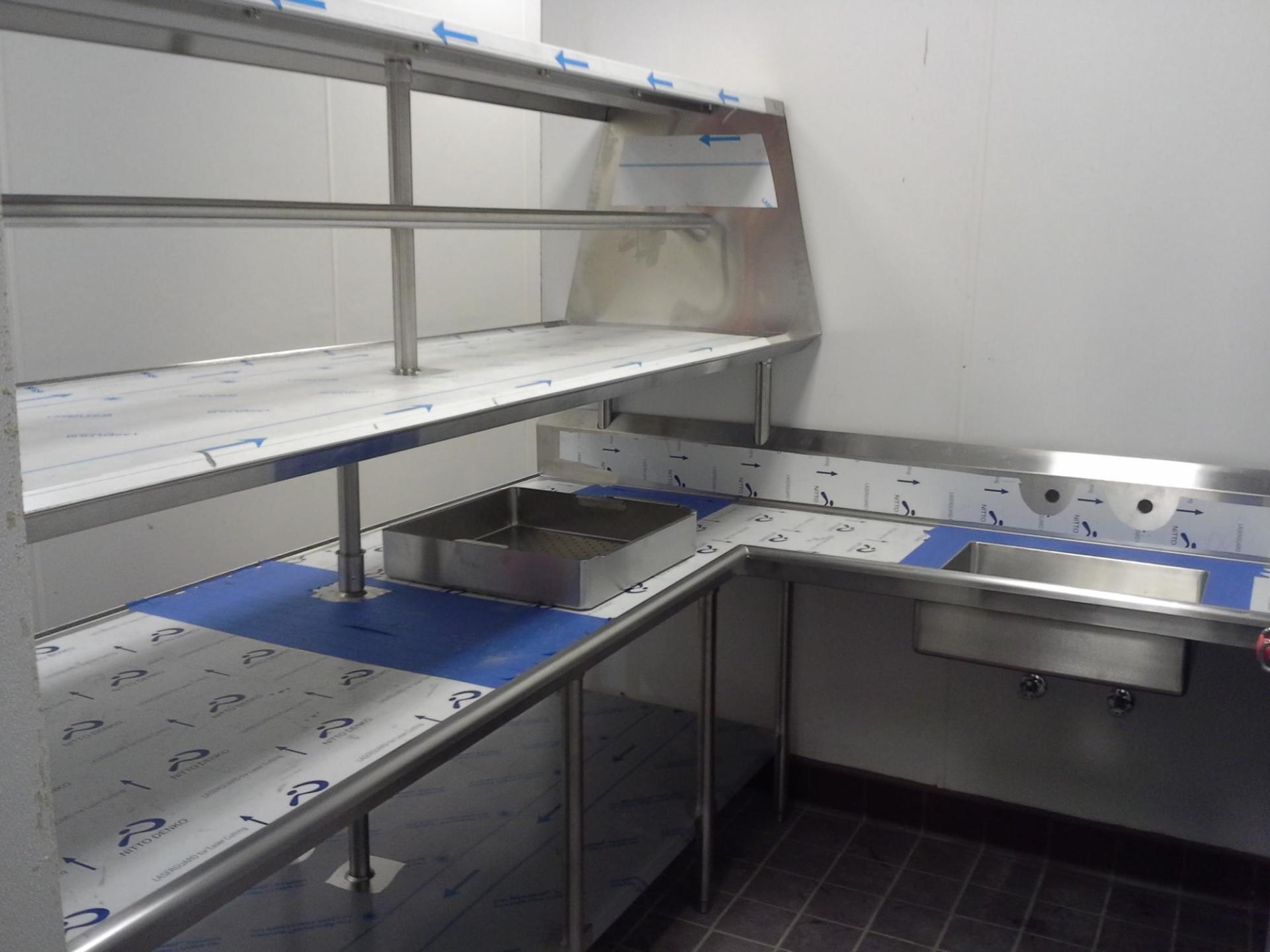 Empty industrial workbench with metal shelving, blue bins, and a stainless-steel counter in a lab or workshop.