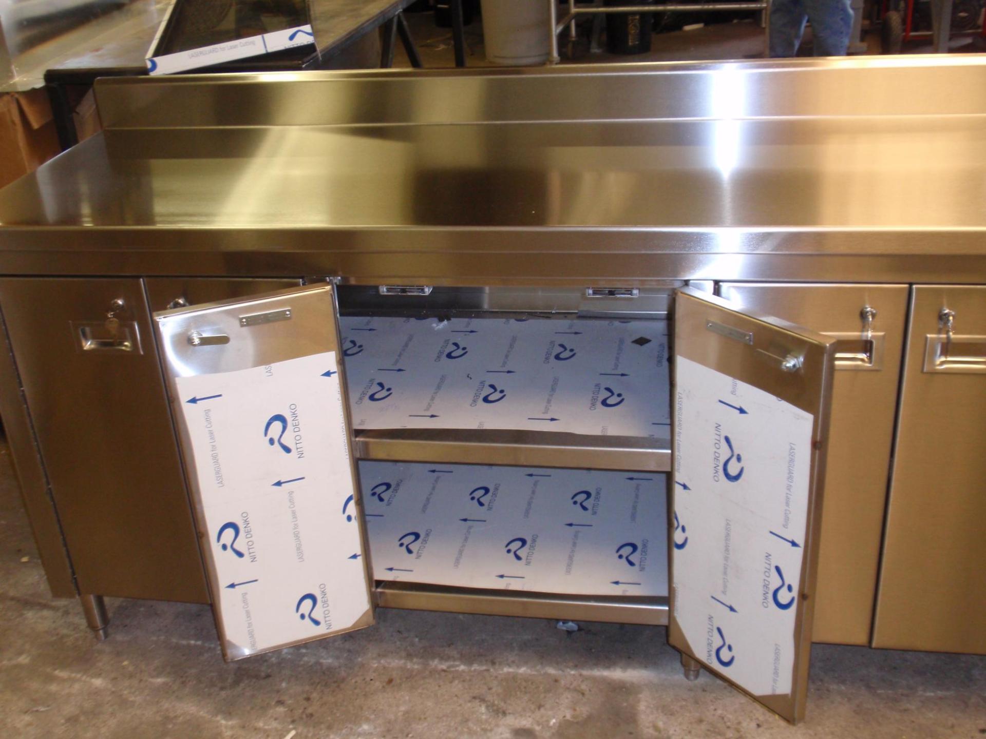 Stainless steel kitchen cabinet with open doors and shelves, unfinished inside with protective film.