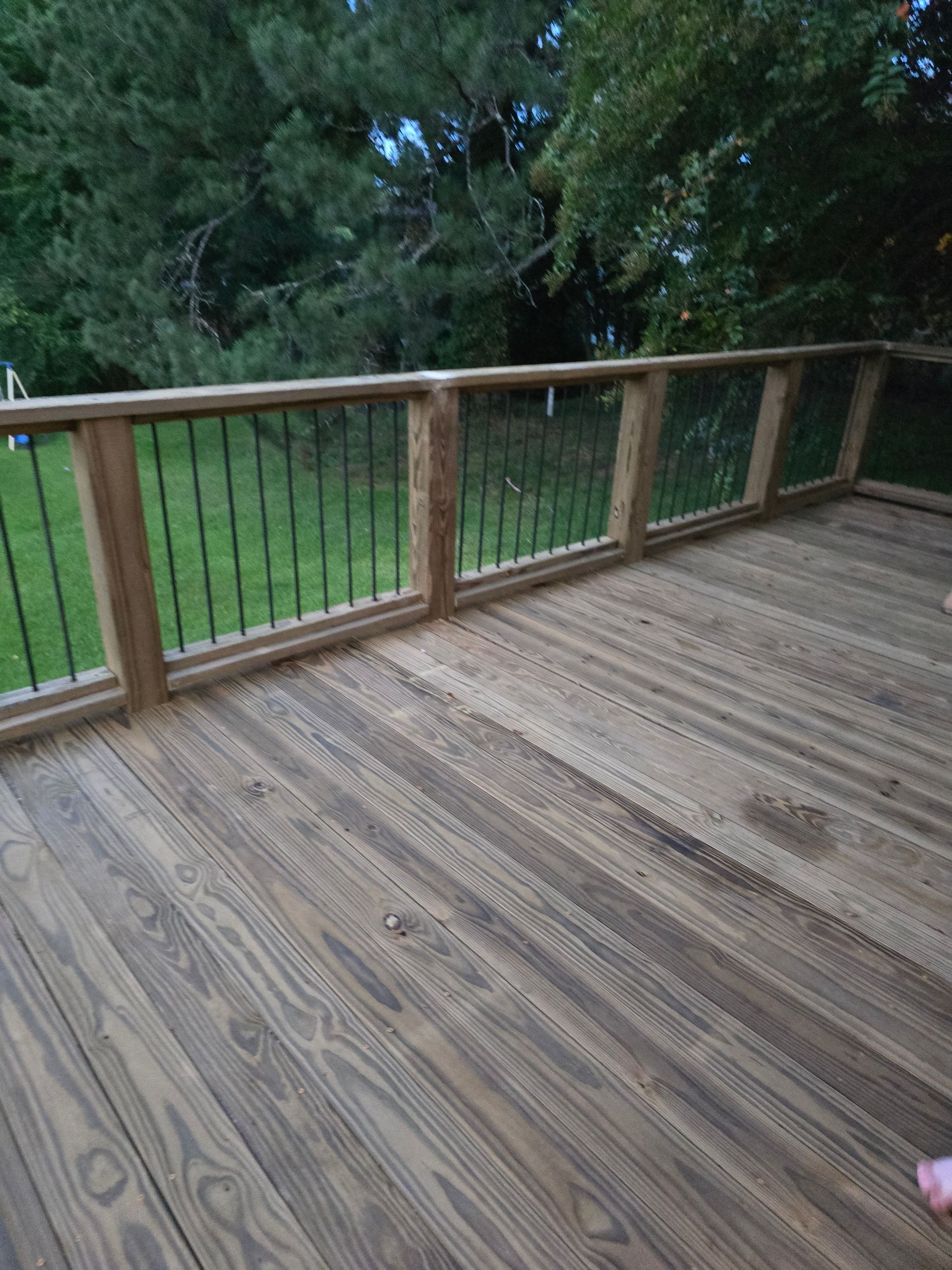 Wooden deck with black metal railing overlooking a grassy yard with trees.