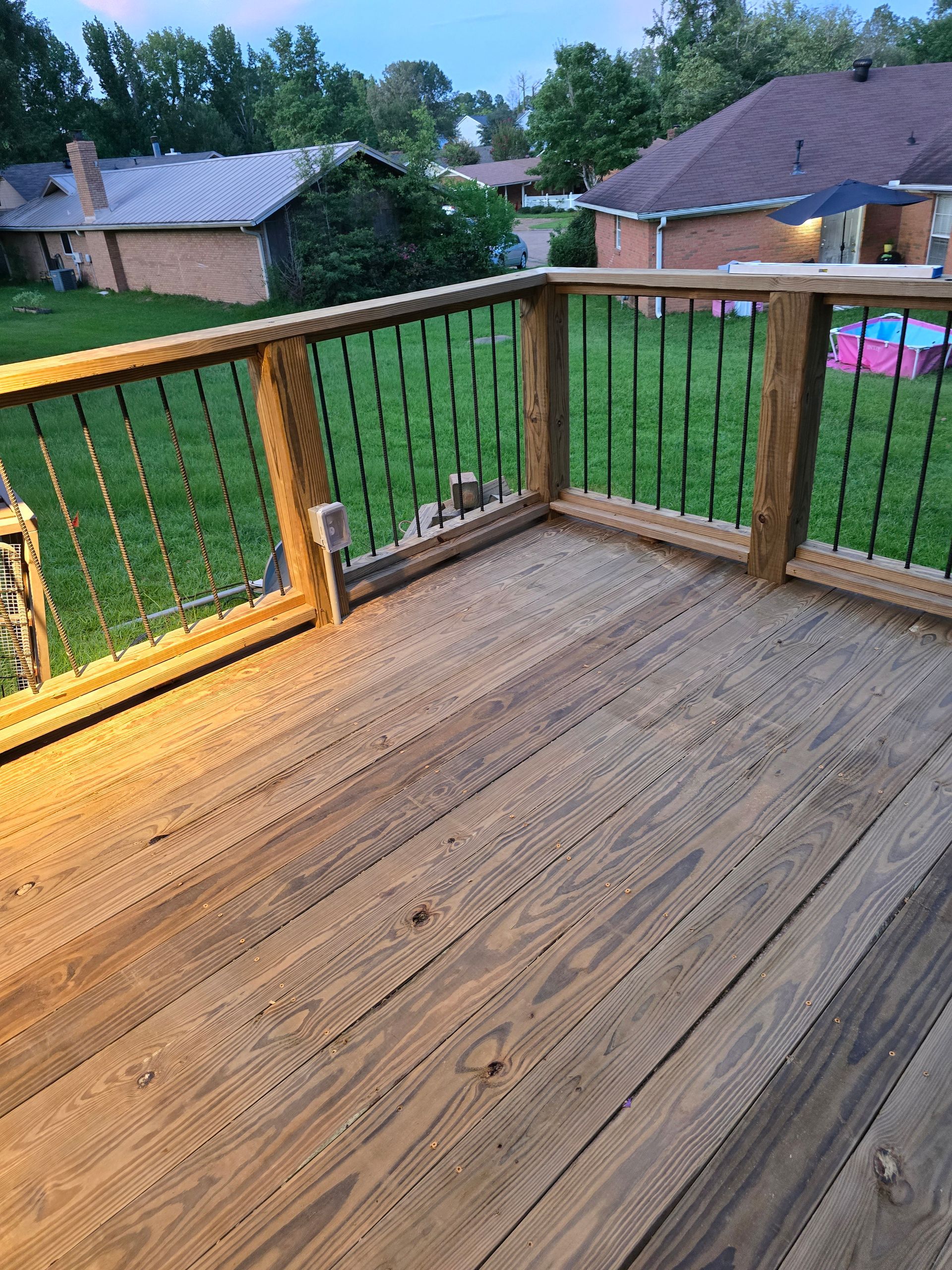 Wooden deck with black railings overlooking a green lawn and houses.