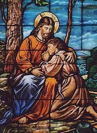 Stained-glass scene of Jesus embracing a kneeling child beside a tree.