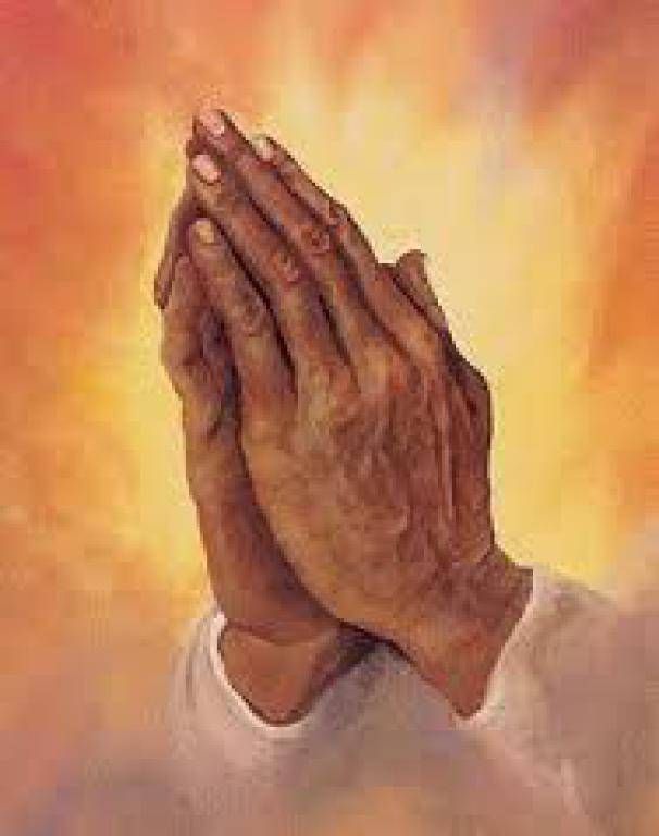 Praying hands clasped in front of a warm glowing background
