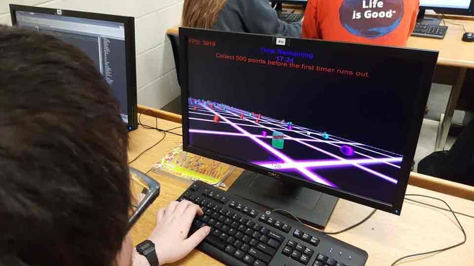 Person using a desktop computer with a black keyboard and a monitor showing a neon grid game scene