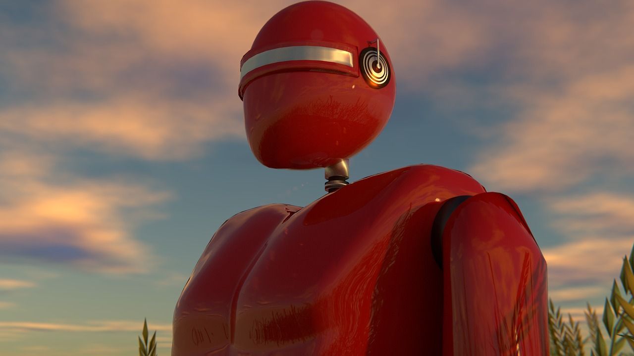 Red humanoid robot with a glossy helmet, standing outdoors against a sunset sky.