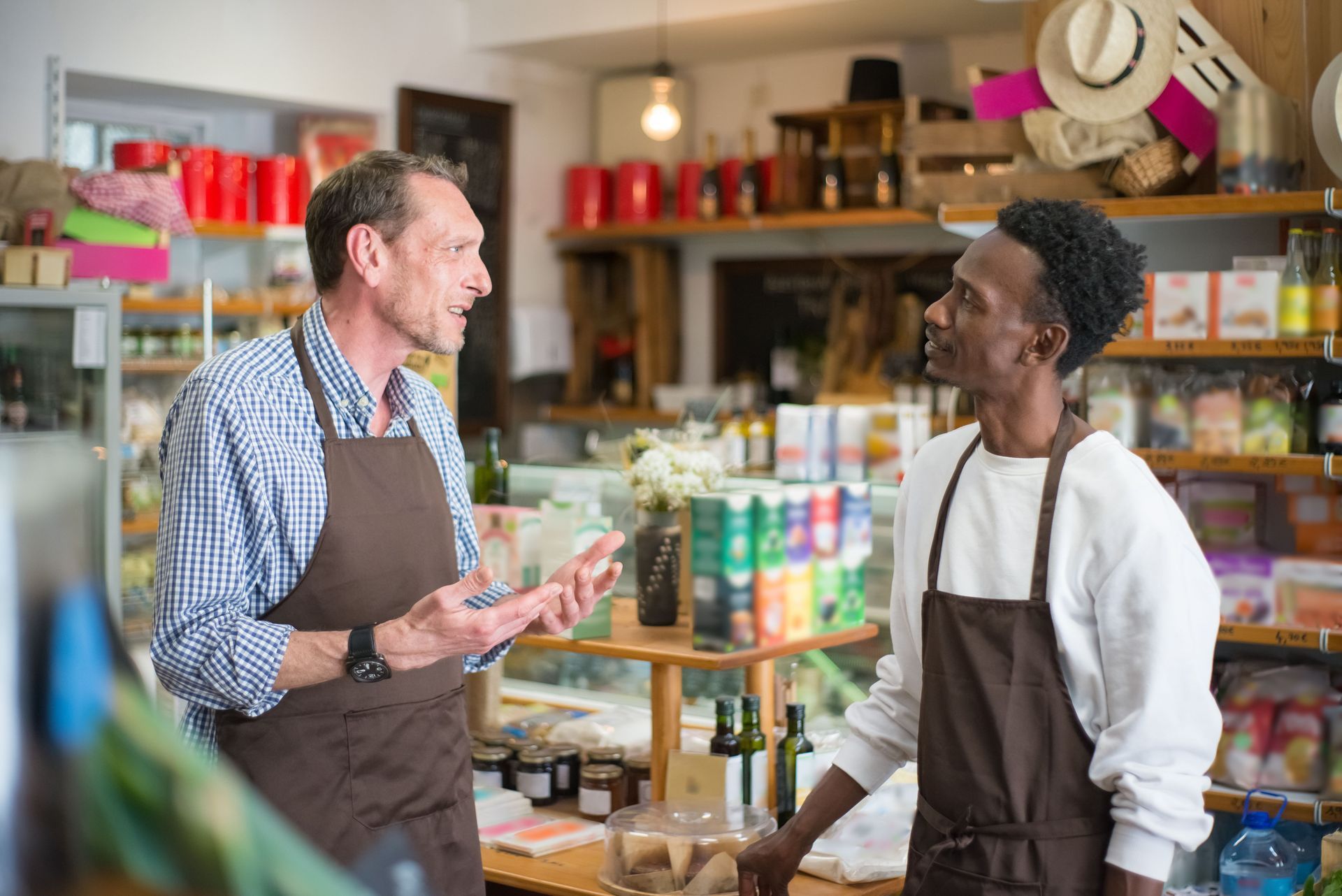 Two people talking in a shop, with shelves of colorful products in the background.