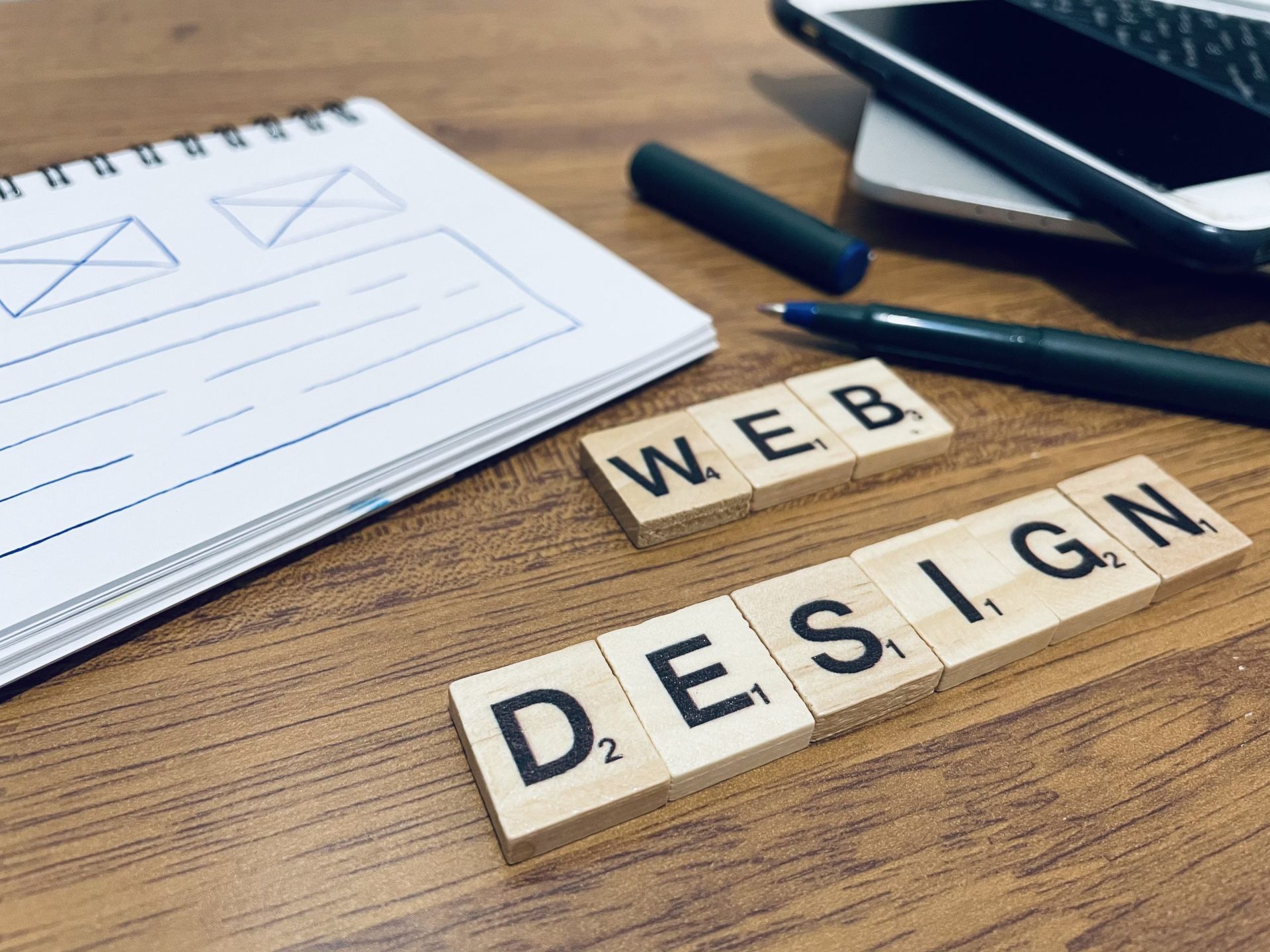 Web design sketch, letter tiles, and a smartphone on a wooden desk