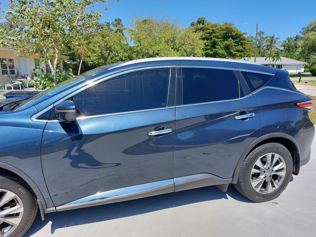 A blue car is parked in front of a house on a sunny day.
