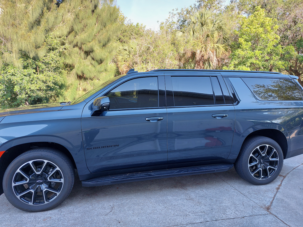 A black suv is parked in a driveway with trees in the background.