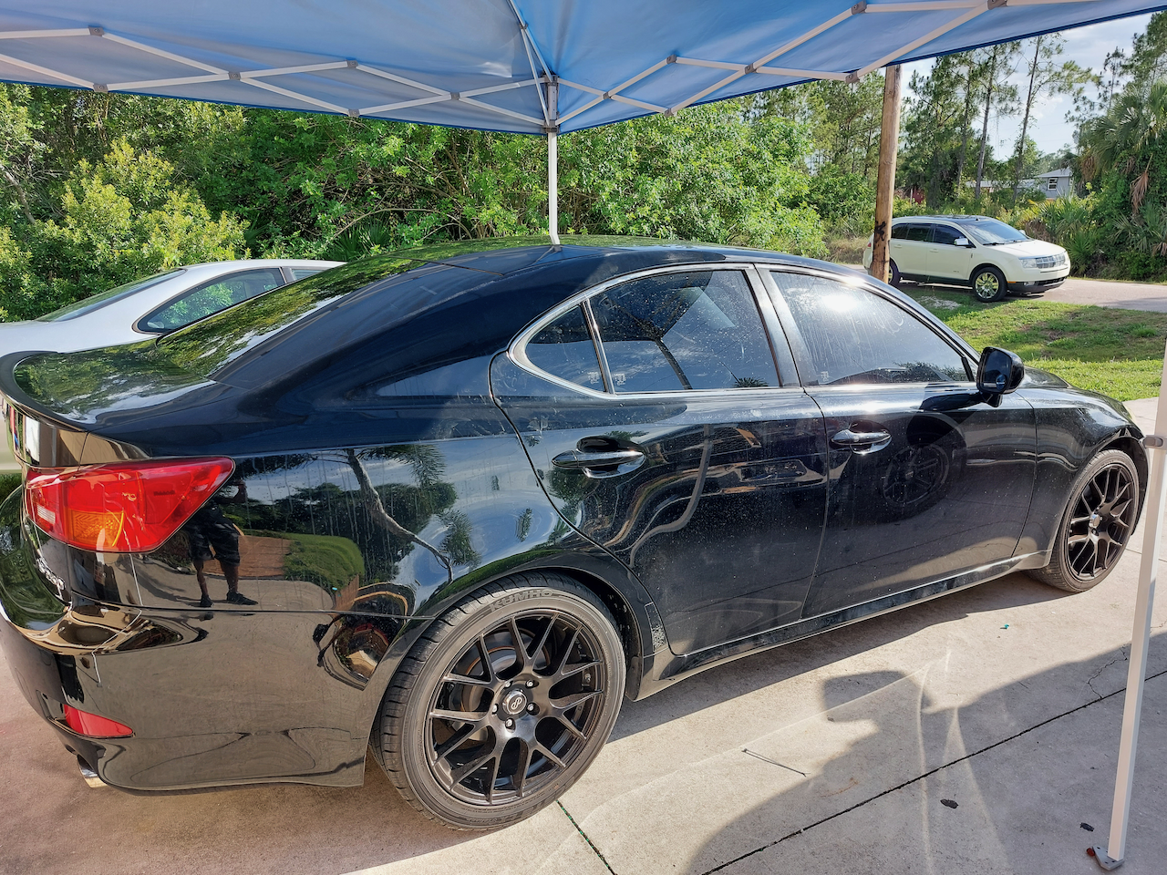 A black car is parked under a blue tent.
