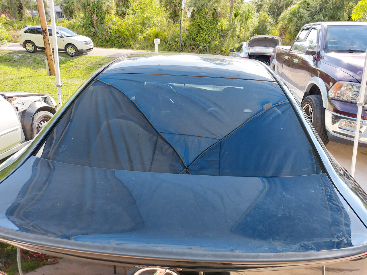A black car with a tent on the windshield is parked in a driveway.