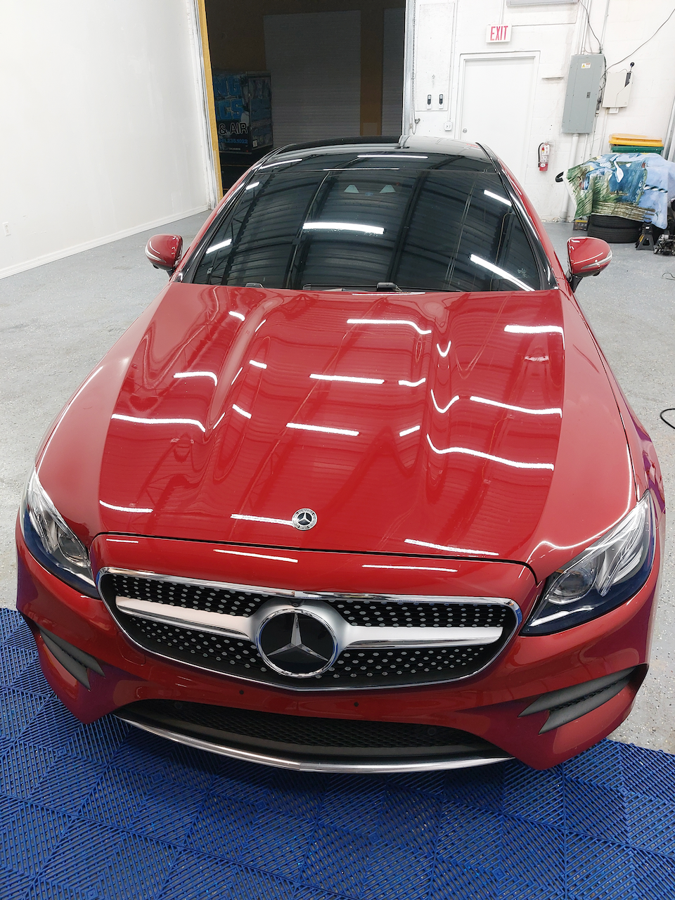 A red mercedes benz is sitting on a blue mat in a garage.