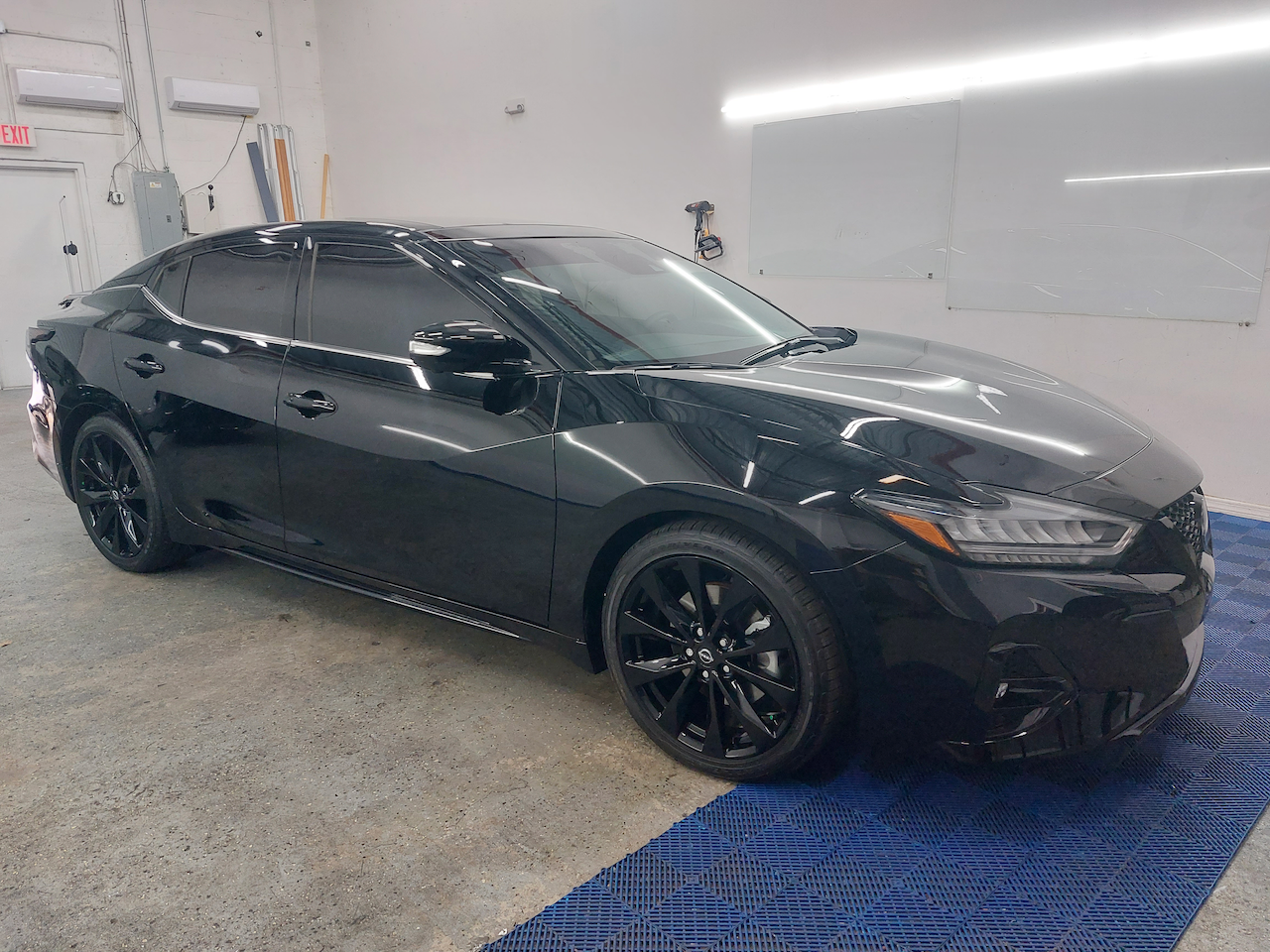 A black car is parked in a garage next to a blue mat.