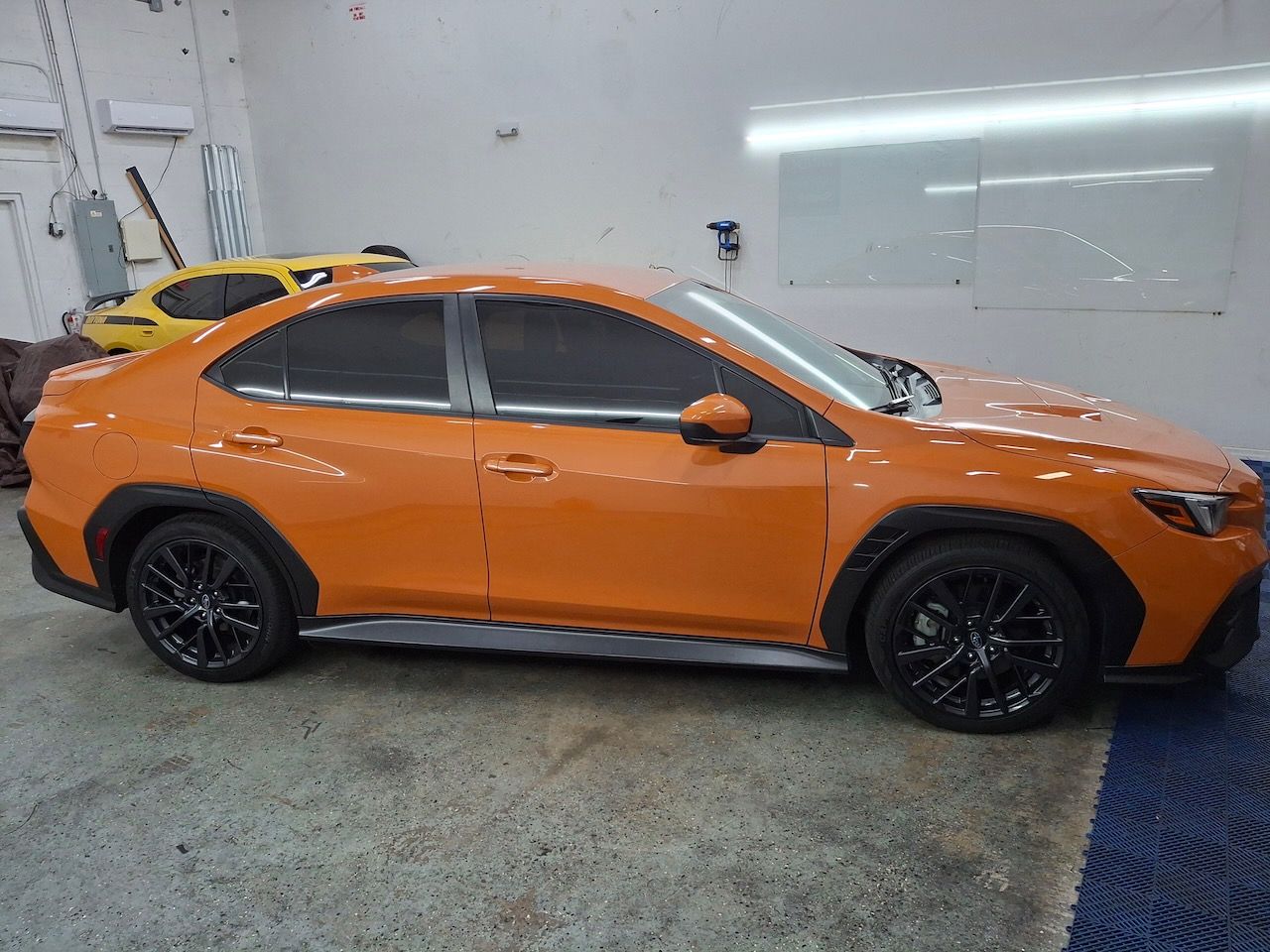 An orange car is parked in a garage next to a yellow car.