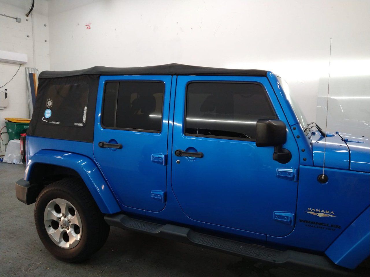 A blue jeep with a black top is parked in a garage