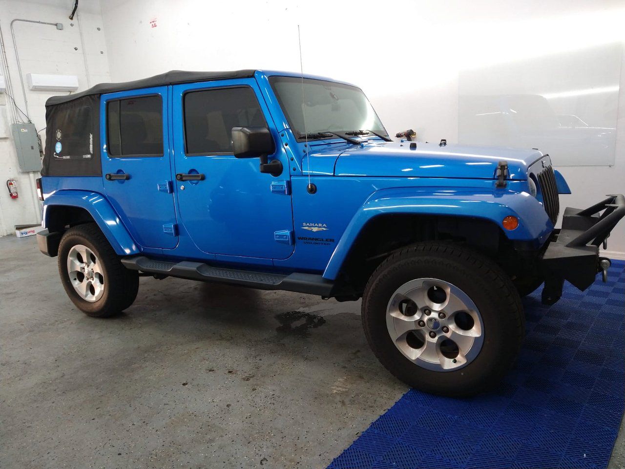 A blue jeep is parked in a garage on a blue mat.