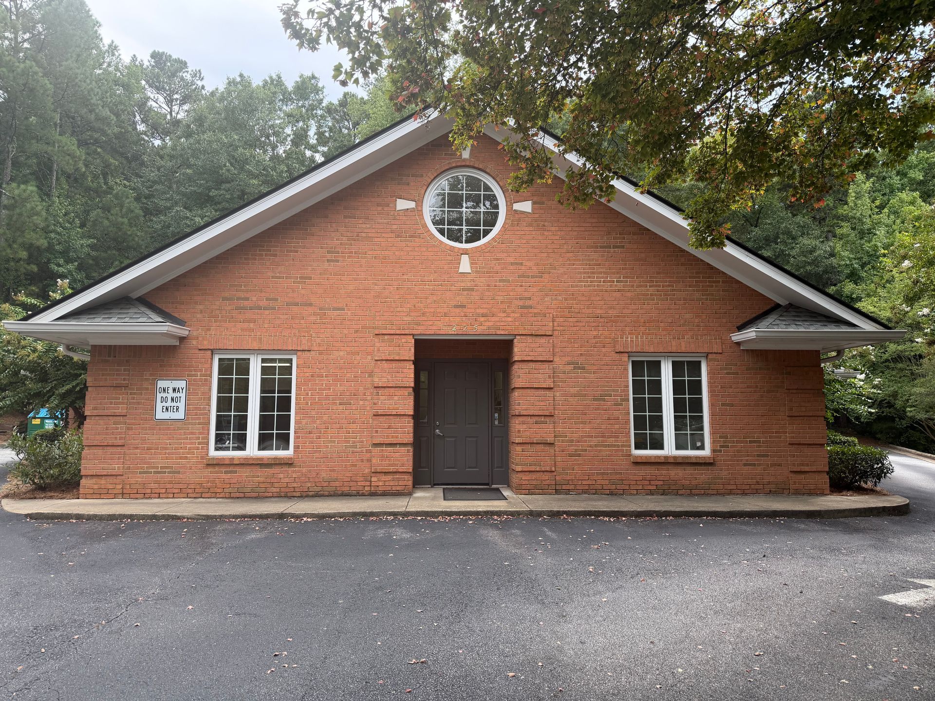 Brick building with a circular window, dark front door, and small windows amid trees