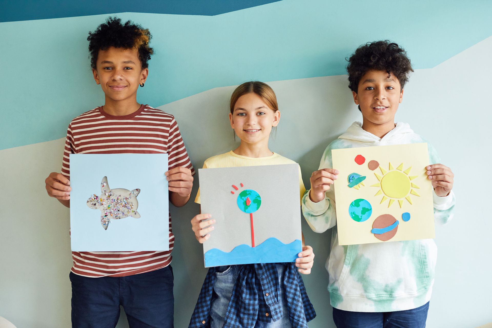 Three children holding colorful drawings against a blue background