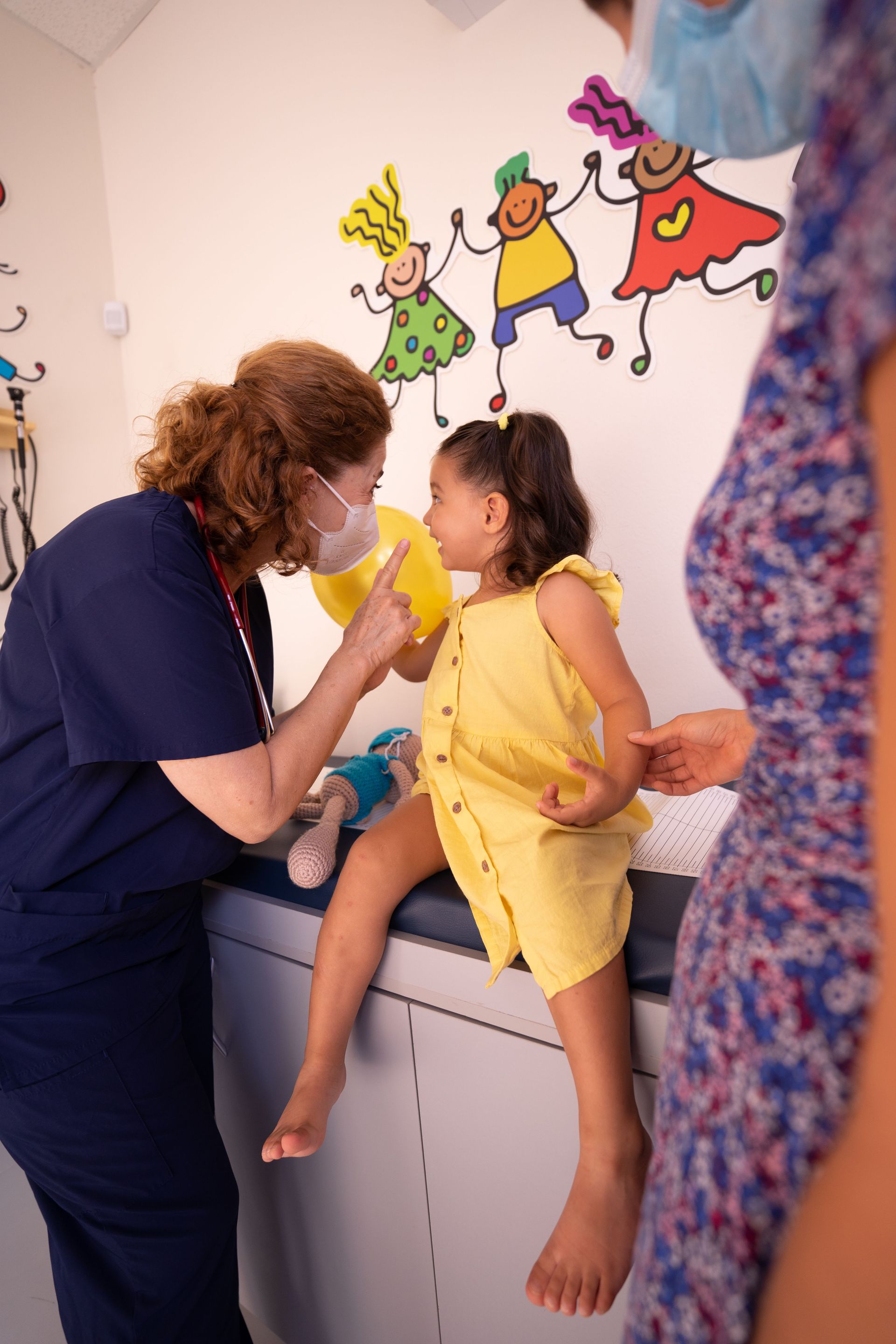 Healthcare worker examining a child in a yellow outfit during a clinic visit