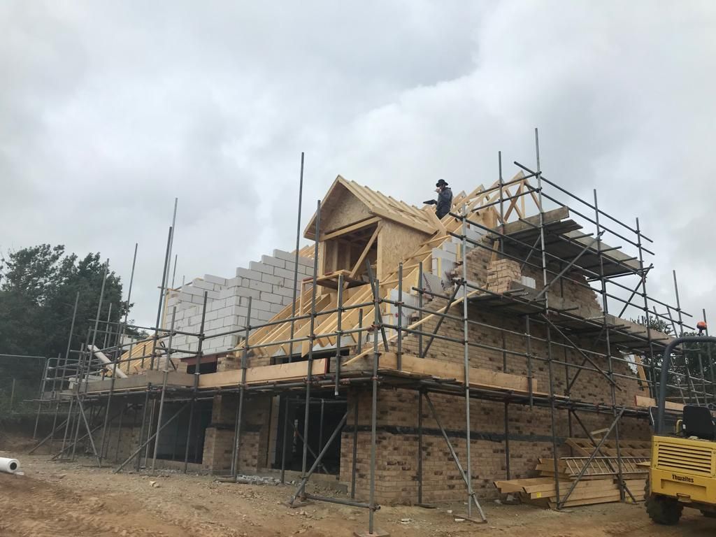 A house is being built with scaffolding and a yellow bulldozer.