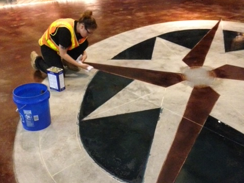 A woman is kneeling down painting a circular pattern on the floor