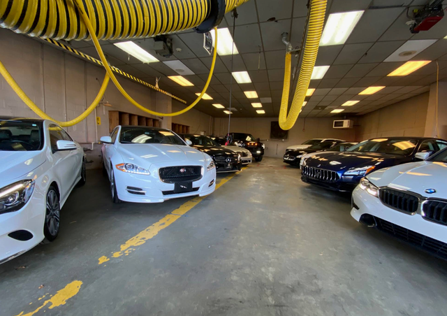 Car showroom with rows of parked cars and yellow exhaust hoses hanging from the ceiling | iDeal Auto Service