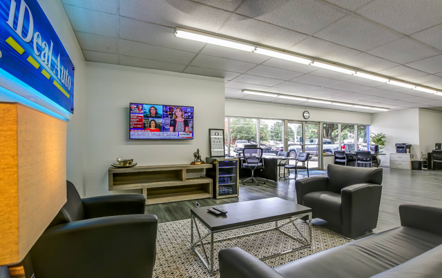 Modern office lounge with couches, TV, coffee table, and glass doors overlooking parked cars | iDeal Auto Service