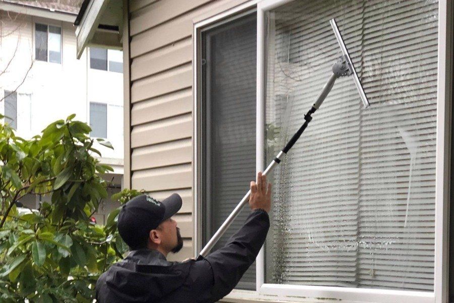 Person washing an exterior window with a long-handled squeegee beside a house