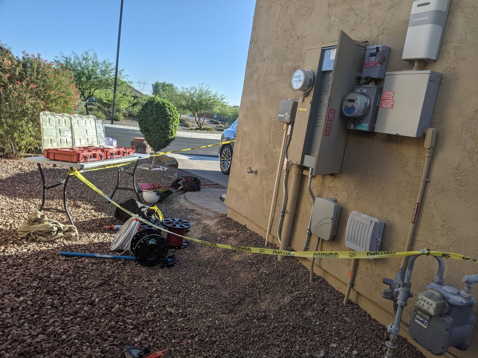 Outdoor utility meters and electrical boxes mounted on a stucco wall beside a paved walkway.