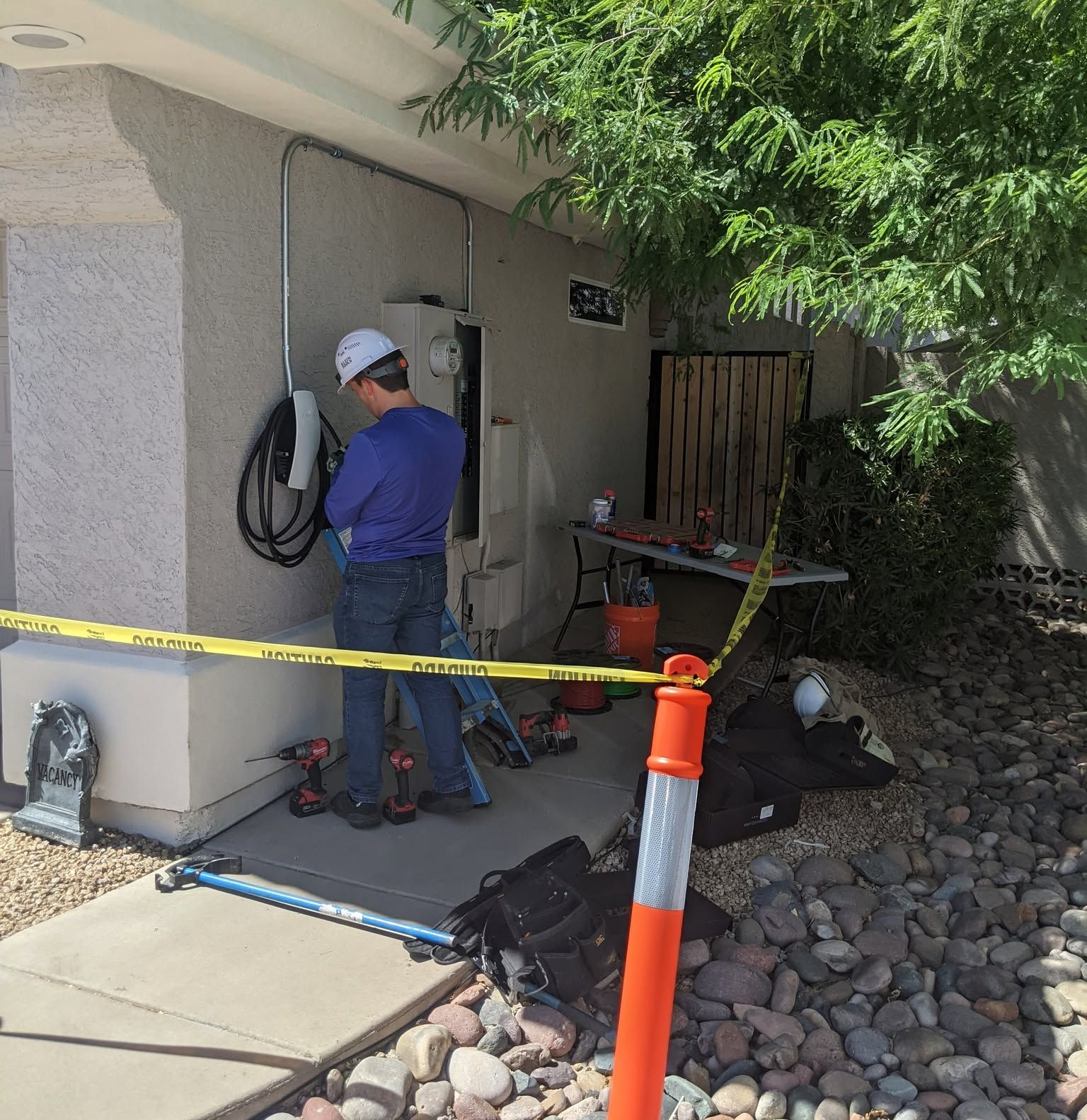 Worker inspecting outdoor wall equipment behind caution tape beside a house.